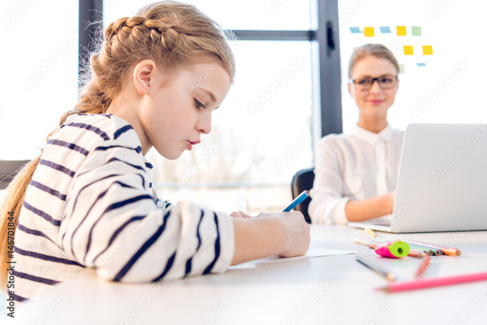 adorable daughter drawing, businesswoman working with laptop behind in office