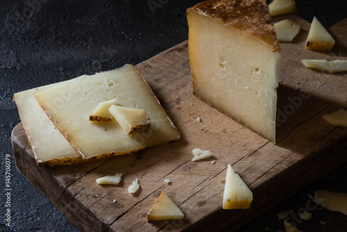 Italian hard cheese pecorino toscano sliced and chopped on wooden board on dark rustic background