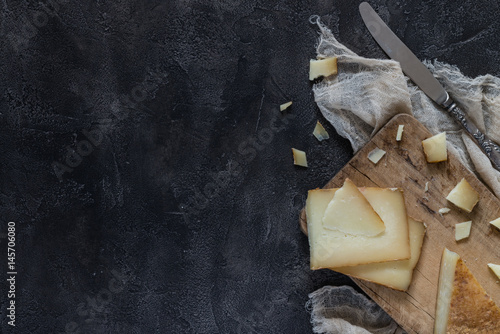 Fototapeta Naklejka Na Ścianę i Meble -  Italian hard cheese pecorino toscano sliced and chopped on wooden board with knife on dark rustic background, top view with copyspace