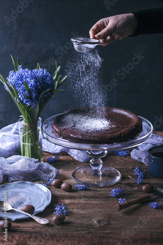 Woman sprinkling powdered sugar on top of Swedish chocolate cake on a cake stand photo