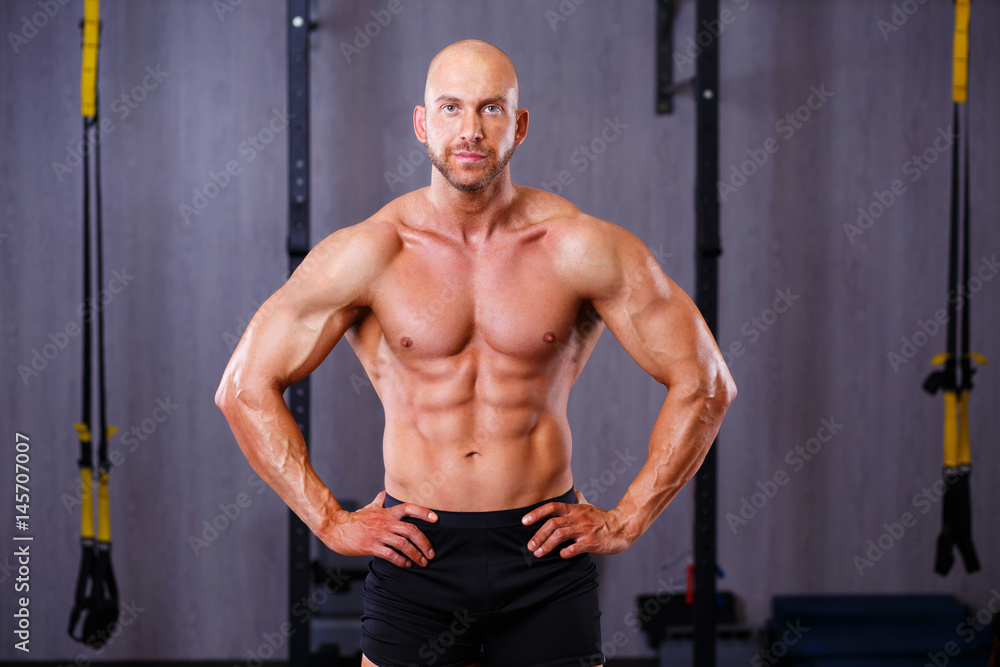 Young healthy bald ripped man with big muscles posing in gym