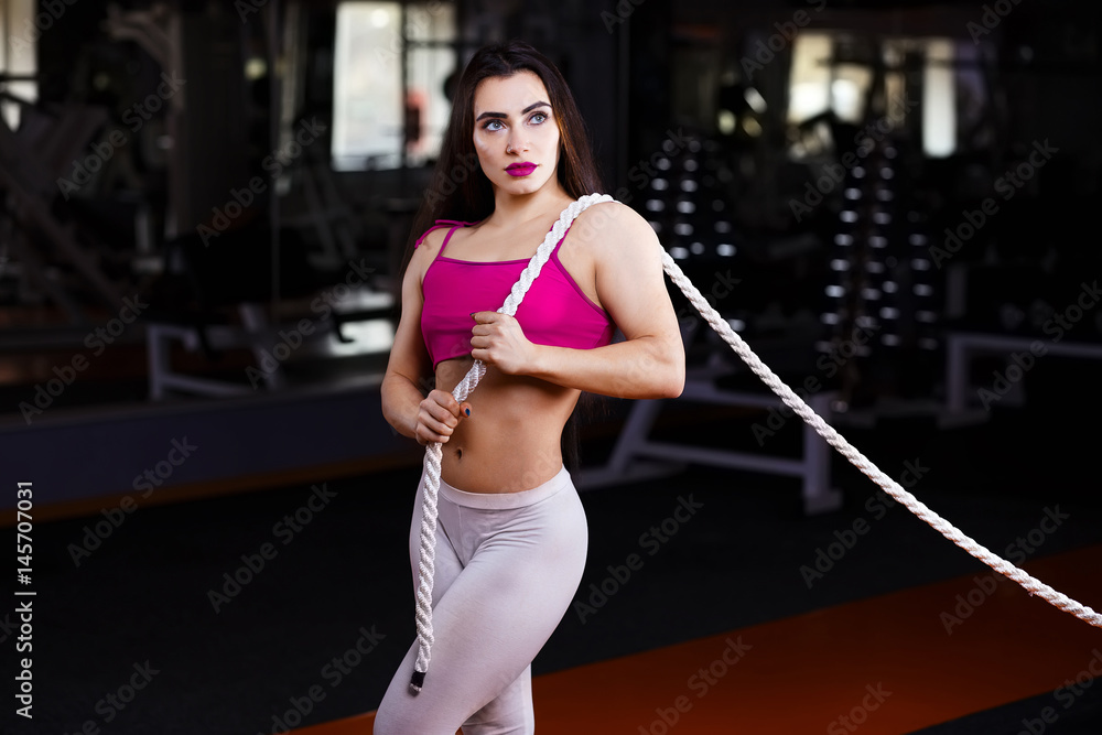 Young attractive muscular sexy fitness woman pulling rope in gym