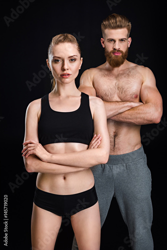 attractive sportswoman and handsome sportsman posing isolated on black in studio