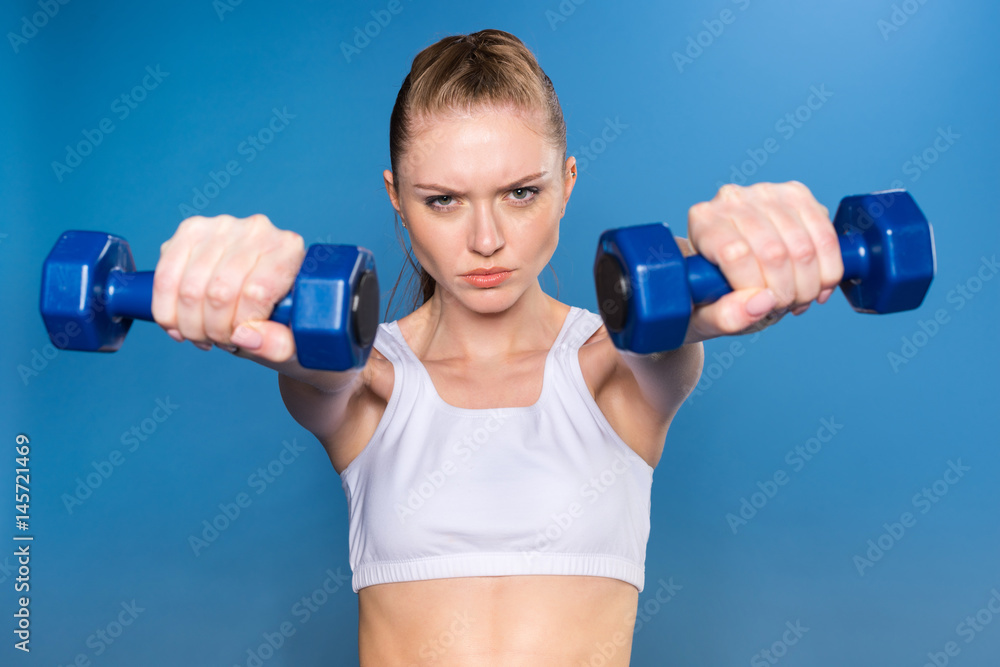 young sportswoman training with dumbbells isolated on blue in studio young sportswoman training with dumbbells isolated on blue in studio
