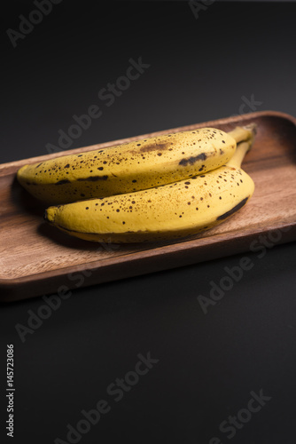 Two organic bananas in a wood sish over a black board. photo