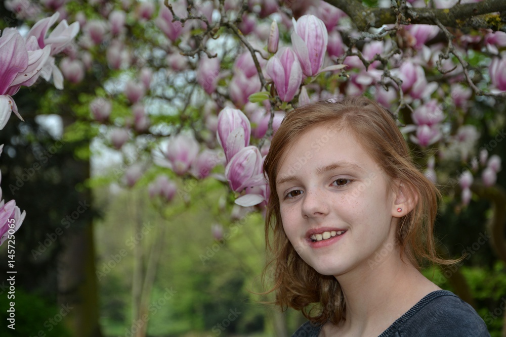 Mädchen steht unter blühenden Magnolienbäumen ( Magnoliaceae ) und lacht nach vorne Mädchen steht unter blühenden Magnolienbäumen ( Magnoliaceae ) und lacht nach vorne