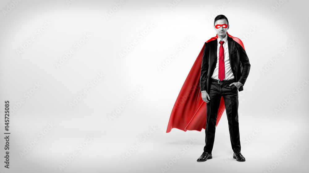 A self-assured businessman in a red cape and a mask standing with a hand in his pocket on white background.