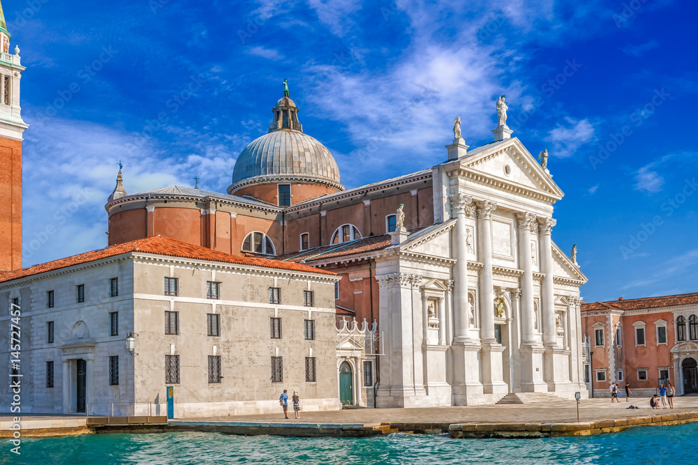 Obraz premium Venice landmark, view from sea of Piazza San Marco or st Mark square, Campanile and Ducale or Doge Palace with some people around with colorful blue sky and white clouds. Italy, Europe.