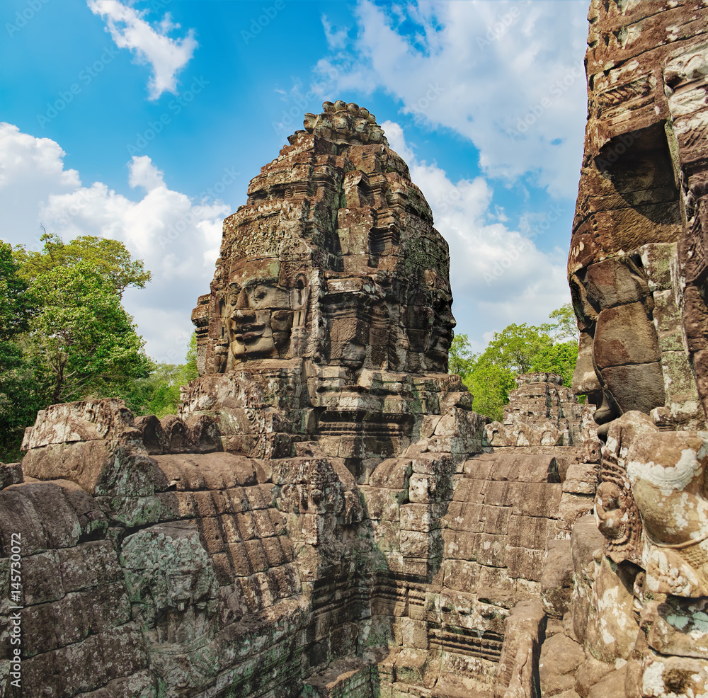 Smiling stone faces of Prasat Bayon, the central temple of Angkor Thom Complex, Siem Reap, Cambodia. Ancient Khmer temple is surrounded by tropical trees, famous Cambodian landmark, World Heritage.