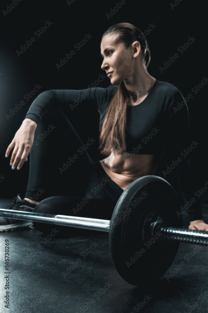 young fitness woman sitting at barbell and resting isolated on black. young fitness woman sitting at barbell and resting isolated on black.