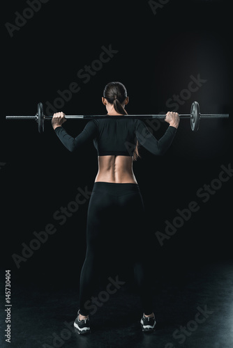 young fitness woman training with barbell isolated on black.