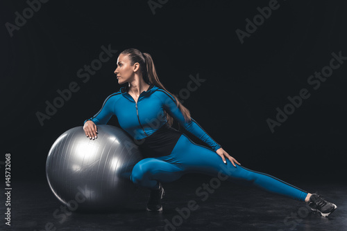 Athletic young woman in sportswear stretching with fitness ball