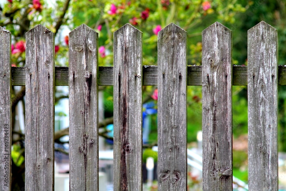 Simple village woody fence on shallow focus flower garden background.