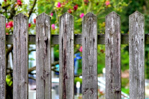 Simple village woody fence on shallow focus flower garden background.