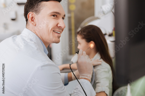 Positive delighted ENT doctor examining ear of little patient