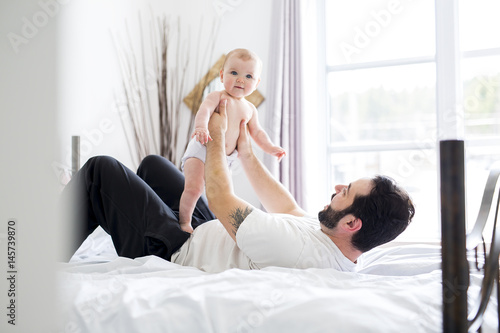 Young happy father playing with babyon bed photo