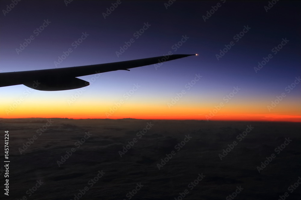 Airplane wing in flight, warn and cold colors through from window, beautiful sunrise light Airplane wing in flight, warn and cold colors through from window, beautiful sunrise light