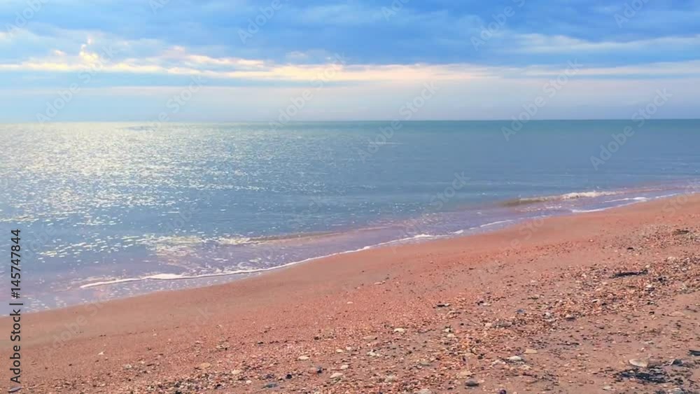 Sea or ocean waves on a deserted beach, blue water and yellow sand under cloudy sky with big, heavy clouds Sea or ocean waves on a deserted beach, blue water and yellow sand under cloudy sky with big, heavy clouds