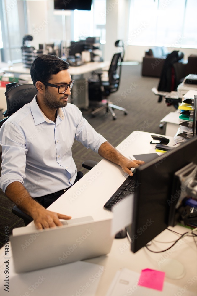 Businessman using laptop and desktop pc together Businessman using laptop and desktop pc together