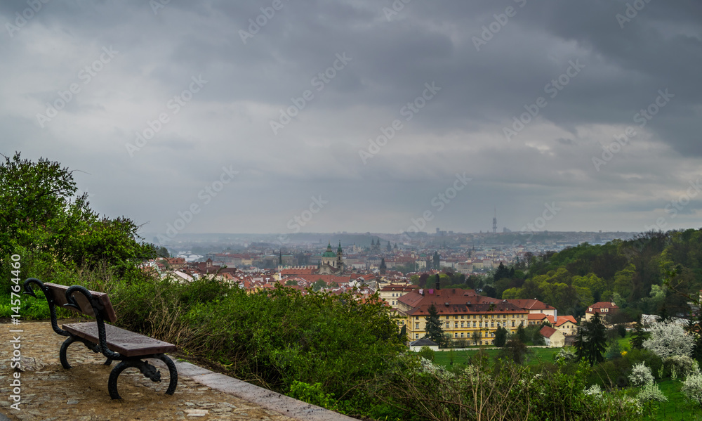 Empty bench on a hill in front of panoramic view on city in rainy day, Prague