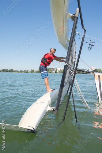 salior trying to right his catamaran after capsize