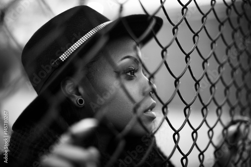 A closeup portrait of a young, attractive, african american woman along a fence in Brooklyn, New York City. Shot in an urban setting during the spring of 2017.