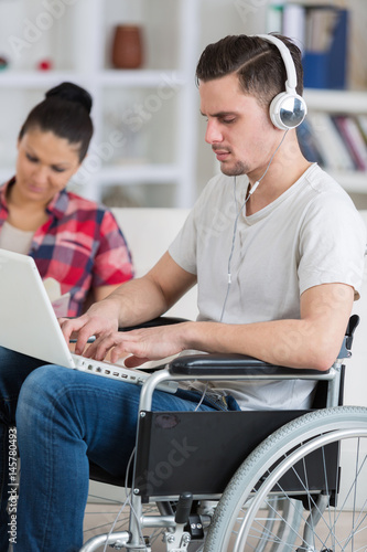 man with laptop on wheelchair with woman aside