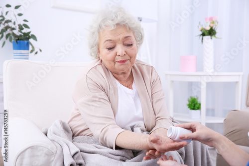 Elderly woman taking pills in light room photo