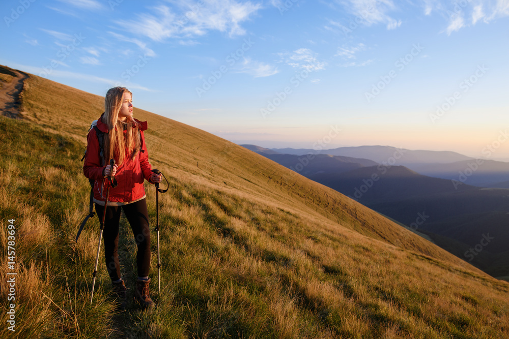Successful woman hiker enjoy the view on mountain top. Travel concept with space for text. Happy traveler with backpack standing on top of a mountain and enjoying sunset view