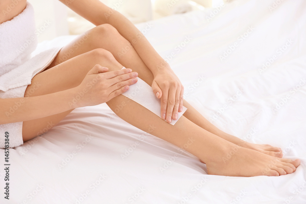 Young woman depilating legs with wax sitting on bed Young woman depilating legs with wax sitting on bed