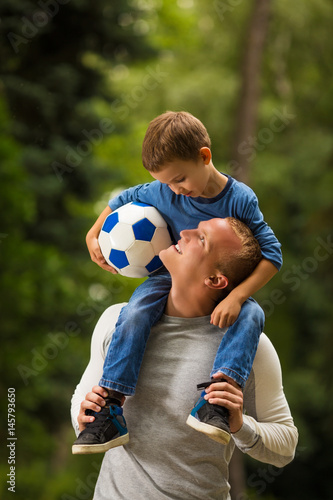 Dad and a little son with a soccer ball walking in park and smiling
