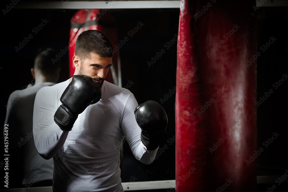 Portrait of young man exercising at the gym. He is practicing with boxing gloves and punching bag