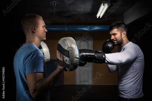 Two young men at the gym are practicing kickboxing punches on punching bag