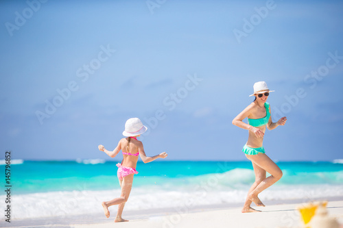 Little adorable girl and young mother haveing fun at tropical beach