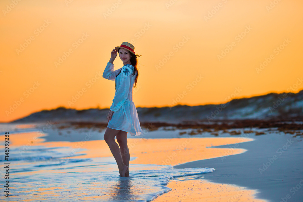 Young beautiful woman on tropical seashore in sunset. Happy girl in dress in the evening on the beach