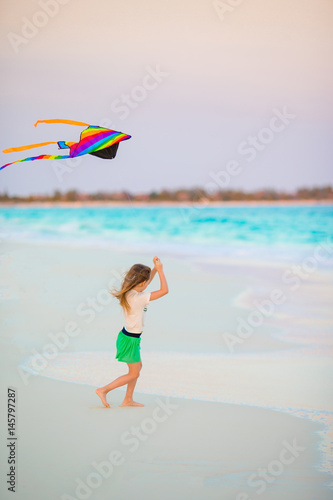 Little girl with flying kite on tropical beach. Kid play on ocean shore. Child with beach toys.