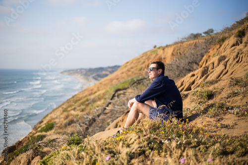 Young man, boy sitting on the cliff in San Diego, California. Sunset cliff. Meditation