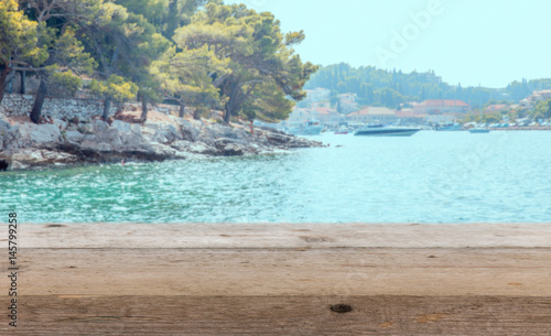 Old wooden table top on blurred blue sea and mediterranean coast with mountains, beach, yacht background - can be used for display or montage your products. Summer holiday background concept .
