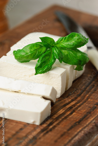 sliced feta cheese decorated with fresh basil leaf on a wooden board. close up and selective focus