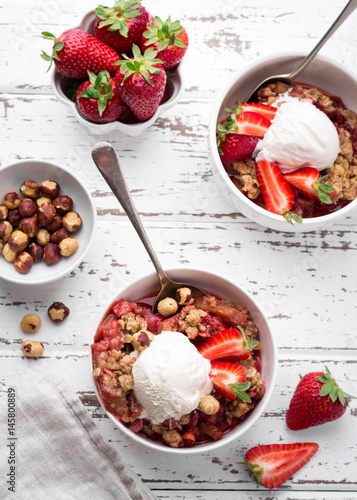 Homemade strawberry and rhubarb crumble  served with fresh berries on light wooden background; Overhead shot