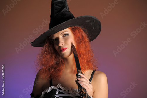 Young woman with red hair in withch costume on dark orange background photo