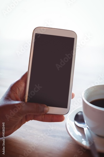 Hand of woman using mobile phone while having coffee