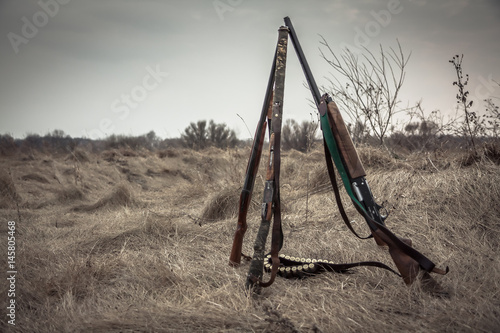 Hunting shotguns in dry rural field in overcast day with dramatic sky during hunting season as hunting background with copy space