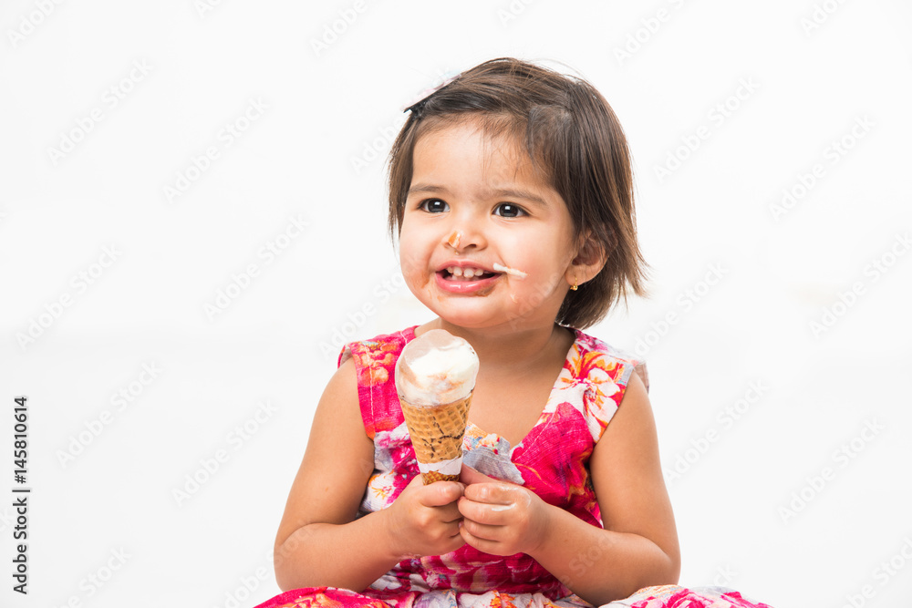 indian adorable infant or girl child licking or eating chocolate ice
