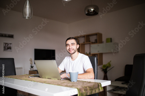 Handsome man with laptop and coffee cup in the kitchen mornings