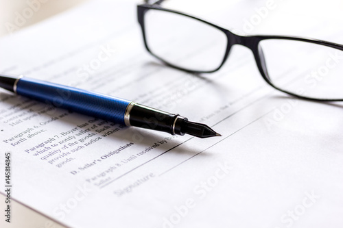 Pen and glasses lying on signed documents on office desk