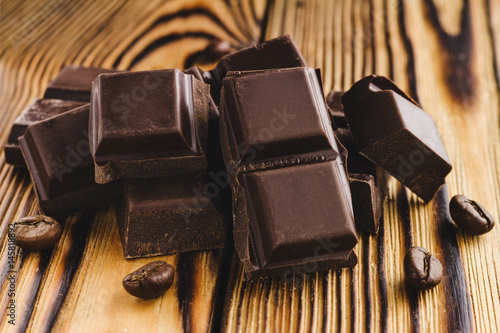 Pieces of bitter, dark chocolate, cubes on heap and coffee bean on wooden background, close-up view
