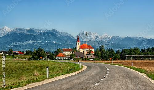 The European landscape where the road leads to the Church building on a background of mountains of Slovenia in Sunny cloudless day horizontal frame