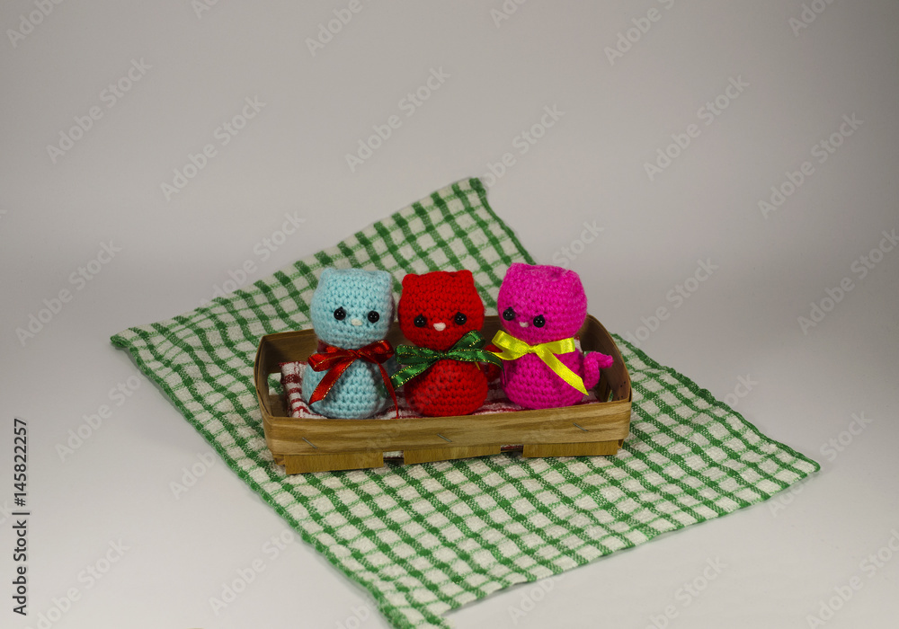 Knitted small red, pink and blue cat on a wicker basket and checkered tablecloth. Handmade. Toy Knitted small red, pink and blue cat on a wicker basket and checkered tablecloth. Handmade. Toy