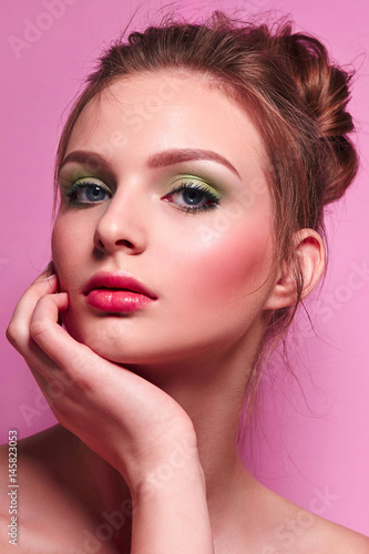 Beautiful young graceful girl with long neck on a pink background in studio. The hair is collected in a high beam. Brown. Fresh bright make-up, green shadows, pink lipstick and blush. Cosmetics. 